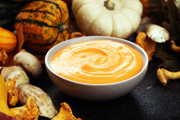 Roasted pumpkin and carrot soup with cream and pumpkin seeds on wooden background.