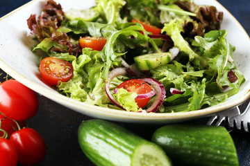 bowl of salad with vegetables and greens, with tomato, cucumber and onions on rustic table