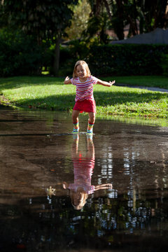A little girl wearing rainbow rain-boots jumping and splashing in her reflection in a puddle