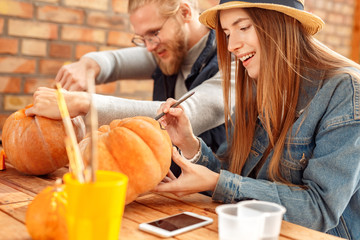 Young adult woman and man decorating ripe pumpkin for halloween