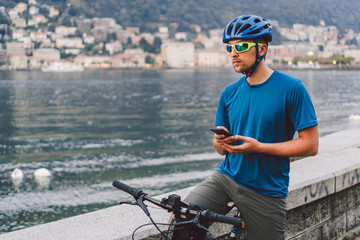 The theme of tourism and travel in Italy. A male cyclist uses a phone on the shore of Lake Como....