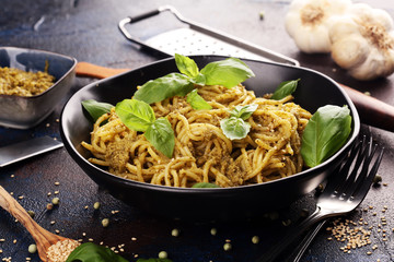 Plate of delicious spaghetti pesto garnished with parmesan cheese and basil on rustic dark background