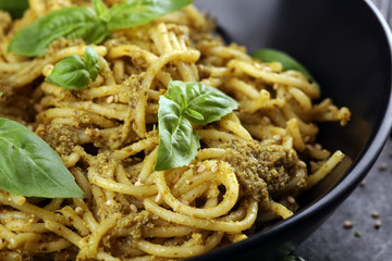 Plate of delicious spaghetti pesto garnished with parmesan cheese and basil on rustic dark background