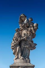 Statue of saint Maria with a child at the Charles Bridge in Prague at blue sky and a pigeon, Czech...
