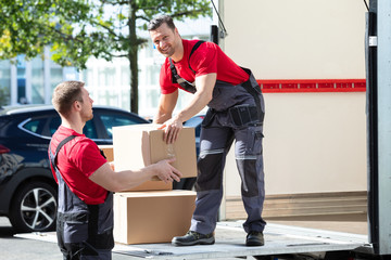 Two Young Male Movers Carrying Cardboard Boxes From Truck