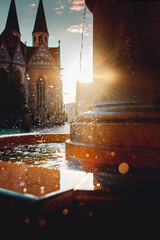 Beautiful old and historic baroque fountain with water reflections and blurry water spray drops in the sunset sun with a dom cathedral in the background. City center, Altstadmarkt in Braunschweig