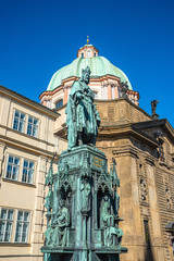 Fototapeta premium Statue of King Charles IV at Charles Bridge Tower and Saint Francis Of Assissi Church in Prague, Czech Republic