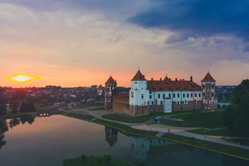 Obraz premium Mirsky Castle and its reflection in the lake in summer. Sunset in cloudy weather with rain clouds.