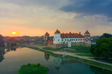 Obraz premium Mirsky Castle and its reflection in the lake in summer. Sunset in cloudy weather with rain clouds.