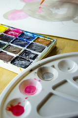 Girl sitting draws with watercolors on a white sheet of paper a mouse with a green gift. Top view. New Year 2020, the year of the mouse