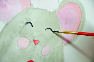 Girl sitting draws with watercolors on a white sheet of paper a mouse with a green gift. Top view. New Year 2020, the year of the mouse