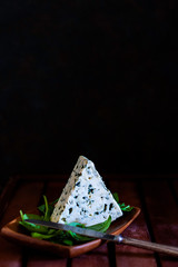 BLUE CHEESE WITH GREEN LEAVES AND KNIFE ON WOODEN DISH