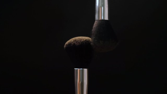 Two black makeup brushes with powder or blush on a dark background. Beauty concept.
