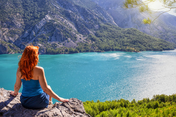 Girl with red hair on cliff top of canyon with green water