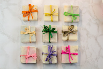 handmade organic craft soap in gift wax wrapping  paper with multi colored eco raffia ribbons on marble surface with space for text. Present gift soap flat lay top view