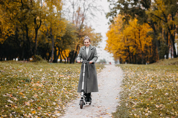 young woman riding an electric scooter in an autumn park. Green transport, traffic jam problems.
