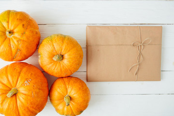 Autumn orange pumpkins with gift in brown paper package tied up with strings on old white wooden background Thanksgiving and Halloween concept. Top view. Copy space for text and design