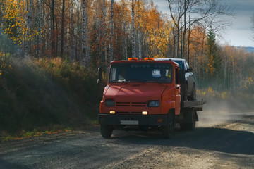 Fototapeta na wymiar Tow truck rides along a forest road against the backdrop of an autumn forest.