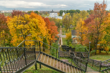Fototapeta na wymiar A long metal staircase among many beautiful autumn trees with bright leaves, in the background a monastery