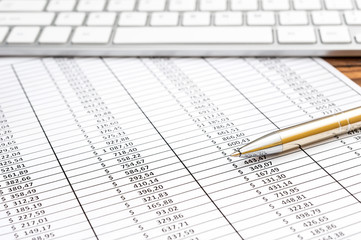Spreadsheet with financial data, pen and computer keyboard on the table. Business concept.