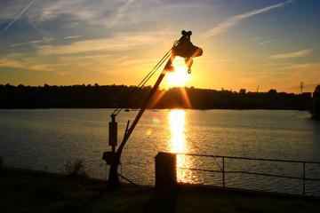 Silhouette of a crane for Marina in against day at sunset in a harbor. View of a lake in the background with reflections of the sun.