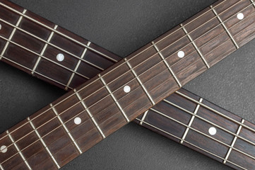 Two fretboard of guitar crossed on black. Close up.