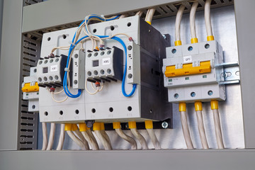 Two powerful electrical contactors or magnetic starters and two circuit breakers in the electrical Cabinet. Power cables and wires are connected to contactors and circuit breakers. Side view.