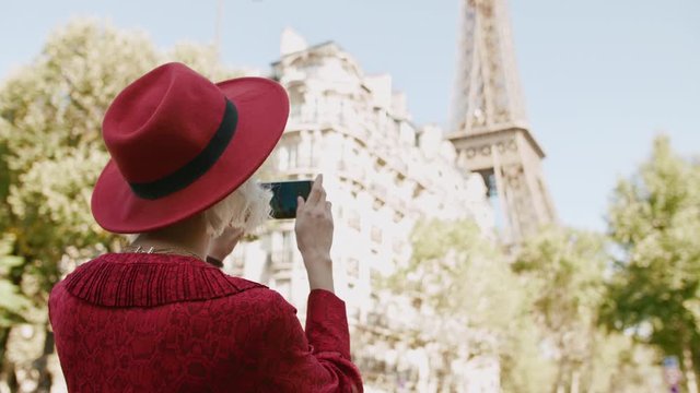 Young fashionable tourist girl in Paris takes photo, makes picture with her smart phone of street with view of Eiffel tower
