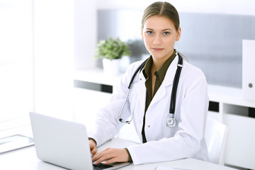 Doctor typing on laptop computer while sitting at the desk in hospital office. Physician woman at work. Data in medicine and healthcare