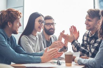 Startupers working together at office having business meeting clapping ot each other joyful