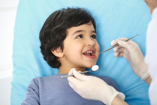 Little arab boy sitting at dental chair with open mouth during oral check up while doctor. Visiting dentist office. Medicine and stomatology concept