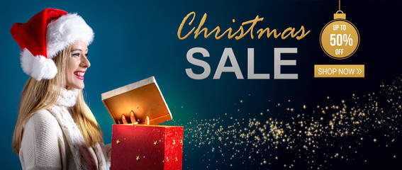 Christmas sale message with young woman with Santa hat opening a gift box