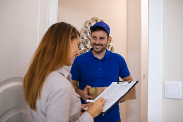 Receiving parcel - delivery man gives package to young woman. View of a Delivery man handing over a parcel to customer. Signing to get her package. Delivery man handing box to woman