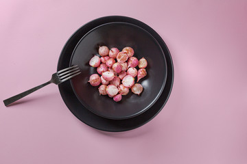 Beautiful roasted radishes in a black plate on pink table close up.