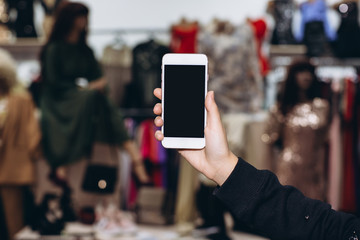 Female hand holding smartphone in clothes shop