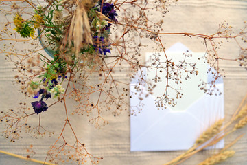 Horizontal rustic composition. Open envelope, white card, dried field flowers and herbs bouquet and ears. Vintage flat lay photo in soft light beige color. Autumn concept. Fall vibes herbarium mock up