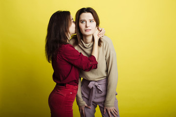 Image of young girls standing isolated on yellow background and sharing secrets