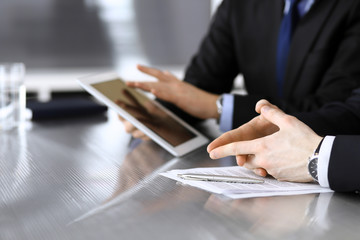 Obraz premium Businessman using tablet computer and work together with his colleague or partner at the glass desk in modern office, close-up. Unknown business people at meeting. Teamwork and partnership concept