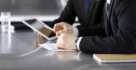 Businessman using tablet computer and work together with his colleague or partner at the glass desk in modern office, close-up. Unknown business people at meeting. Teamwork and partnership concept