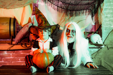 Family party on Halloween. Grandpa and grandson with pumpkin together as preparation for Halloween. Dad and his kid in carnival costumes on Halloween background.