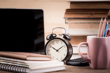 Naklejka premium Alarm clock close up on reading table with old stacked book. vintage filter