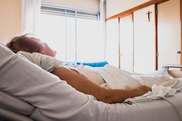 Older woman lying in hospital bed alone looking at the Christian crucifix asking for her healing.