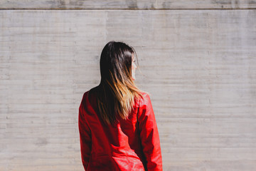 Pretty young woman with smooth and thin hair, with her back to the camera and sad gesture, neutral gray cemetery background with copy space.