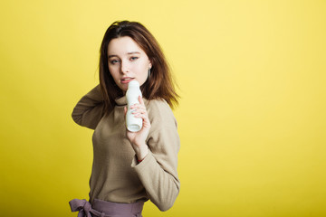 Image of a happy young girl standing isolated on a yellow background singing in a yogurt bottle