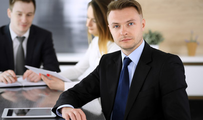 Businessman headshot at meeting in modern office. Unknown entrepreneur sitting with colleagues at the background. Teamwork and partnership concept