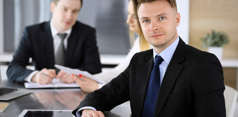 Businessman headshot at meeting in modern office. Unknown entrepreneur sitting with colleagues at the background. Teamwork and partnership concept