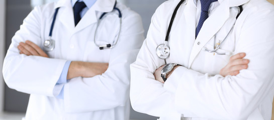 Group of modern doctors standing as a team with arms crossed in hospital office, close-up. Physicians ready to examine and help patients. Medical help, insurance in health care, best treatment and