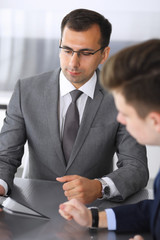 Business people at meeting. Businessman using tablet computer and work together with his colleague or partner at the glass desk in modern office. Teamwork and partnership concept. Grey blazer suits to