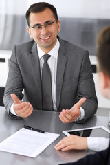 Businessman headshot at meeting in modern office. Entrepreneur sitting at the table with colleagues. Teamwork and partnership concept. Grey blazer suits to happy smiling manager
