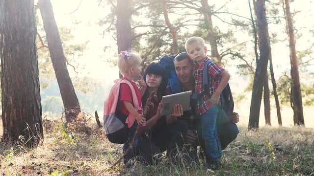 happy family navigation tourists teamwork slow motion video concept. mom dad son and daughter hiking lifestyle in the forest looking for a way on a digital tablet. group of people hikers with